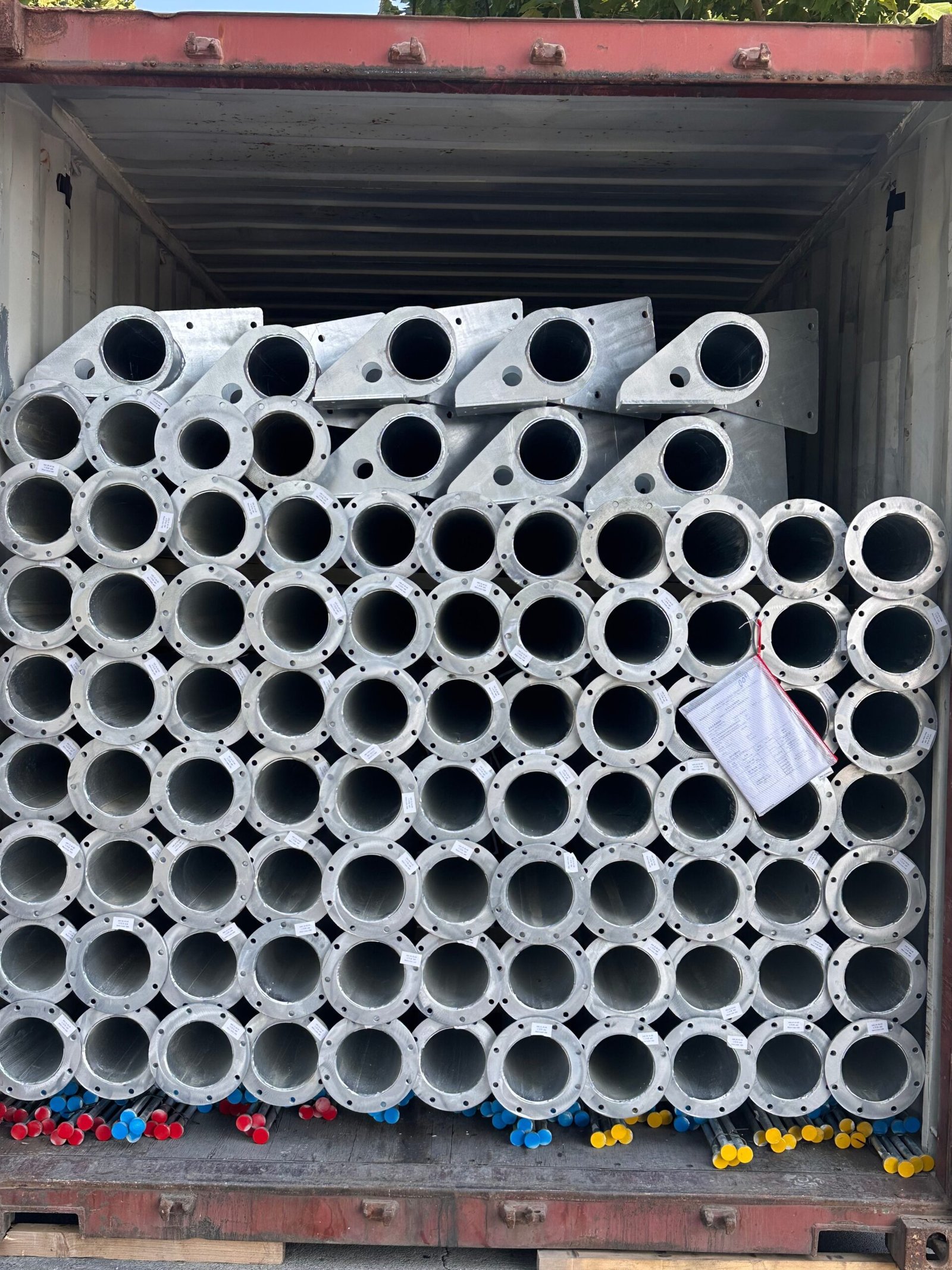 A shipping container filled with stacked metal pipes, each featuring a circular flange with bolt holes at one end.